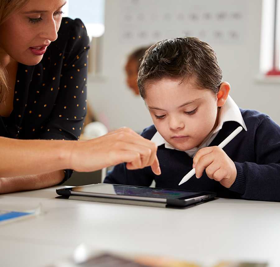 A young boy with down syndrome works with his teacher on an iPad.